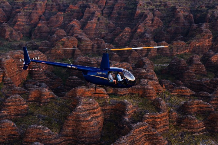 Blue helicopter flying over striped rock formations at sunset.