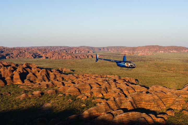 Helicopter flying over expansive desert landscape with rocky formations.