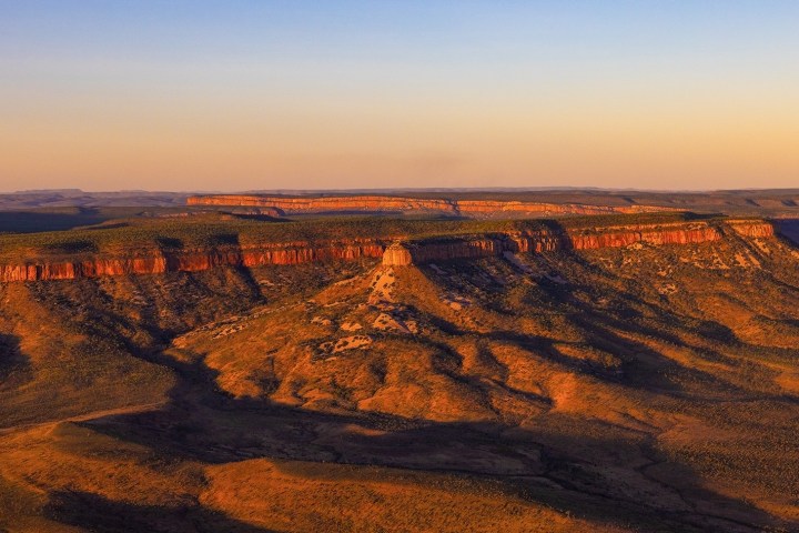 Aerial view of rugged red rock formations at sunset with vast plains in the background.