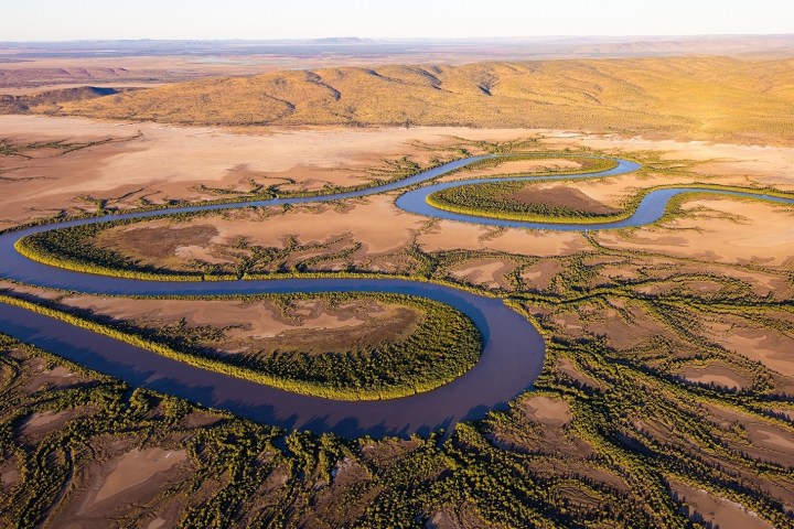 Aerial view of a winding river through a vast desert landscape with scattered greenery.