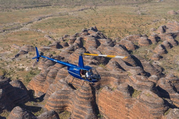 Blue helicopter flying over striped rock formations in a desert landscape.