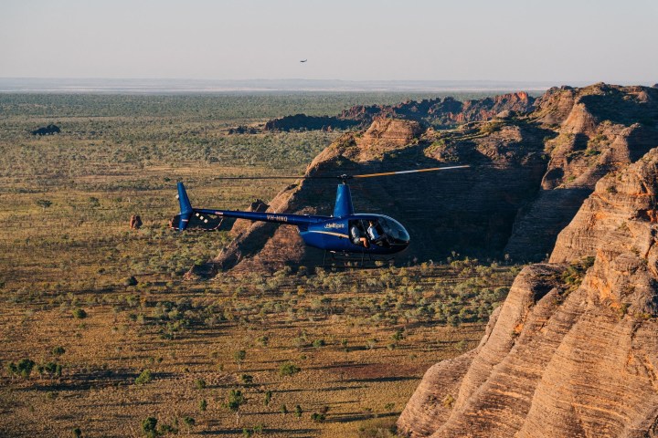 Helicopter flying over rugged rocky landscape with flat plains in the background.