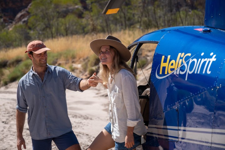 Two people smiling next to a blue helicopter labeled 'HeliSpirit'.