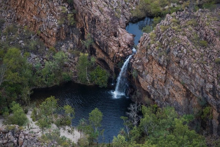Waterfall flowing into a rocky pool surrounded by greenery and cliffs.
