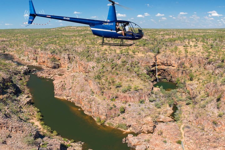Blue helicopter flying over a deep canyon with a winding river.
