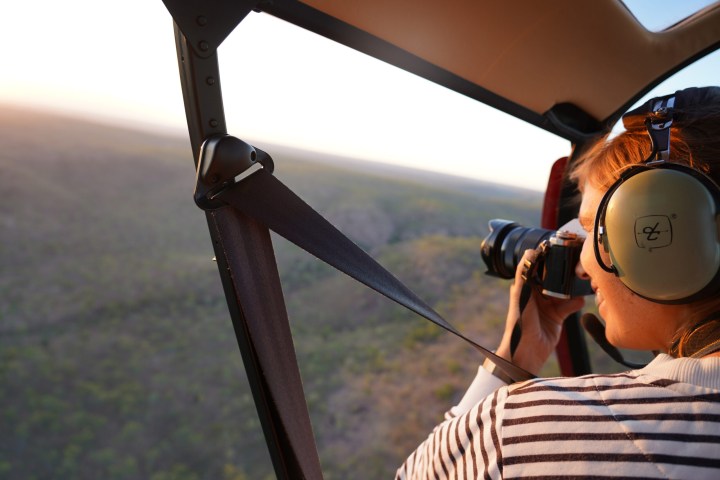Person in helicopter photographing landscape with camera.