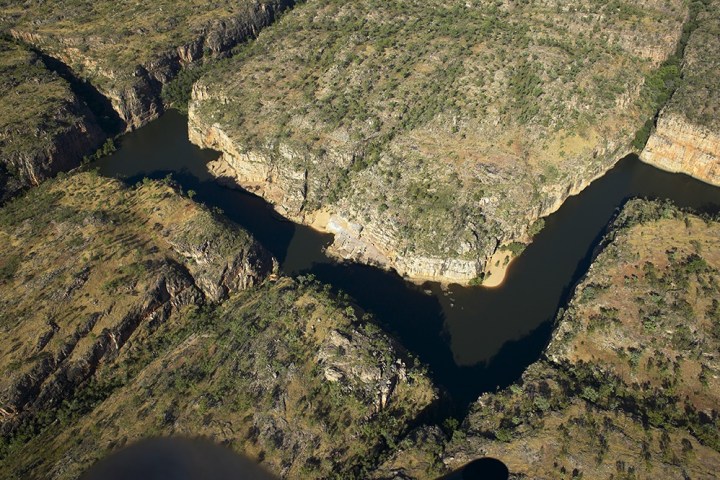 Aerial view of a winding river cutting through rocky terrain and greenery.