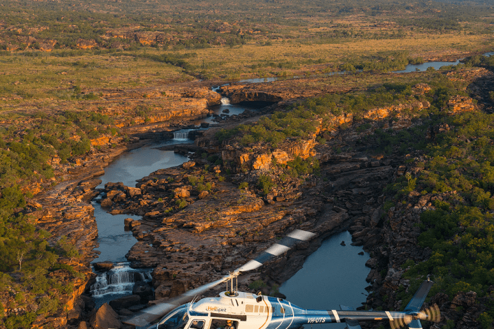Helicopter flying over a canyon with flowing river and rocky landscape.