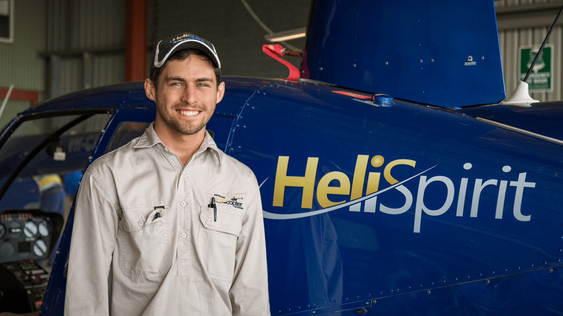 Man in uniform smiling in front of a blue helicopter indoors.