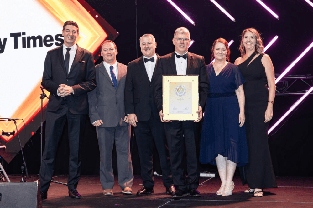Six people in formal attire standing on a stage holding an award.
