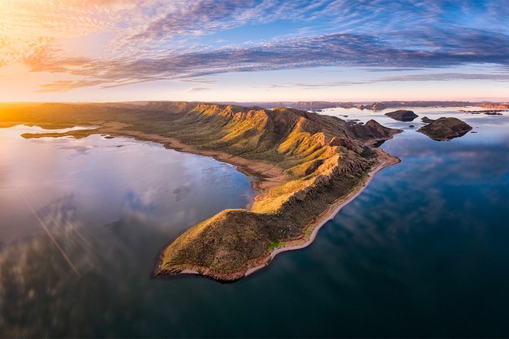 Aerial view of a peninsula with mountains surrounded by blue water and a sunset sky.