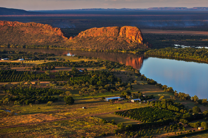 Aerial view of a river alongside farmland and rocky hills during sunset.