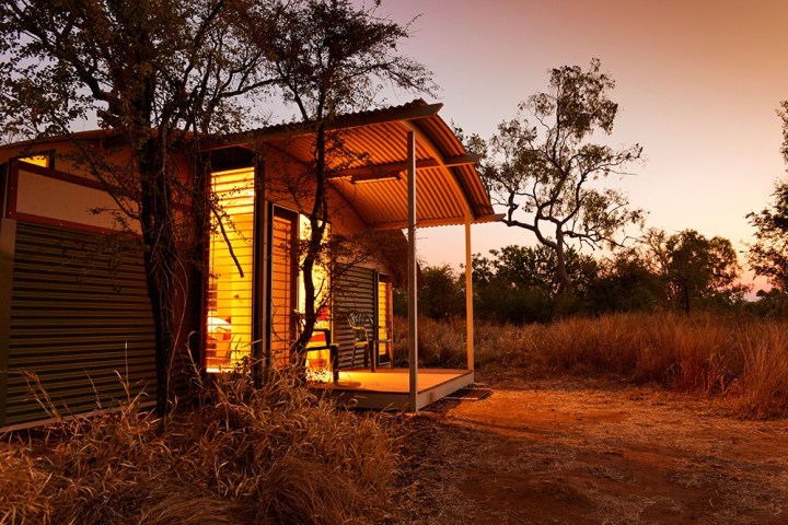 Glowing cabin with open door in a rural landscape at sunset.