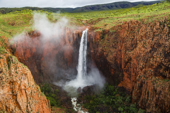 Tall waterfall plunging into a rocky gorge with mist and lush greenery.