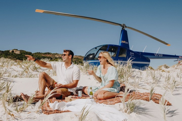 Couple having a picnic on sandy beach with helicopter in background.