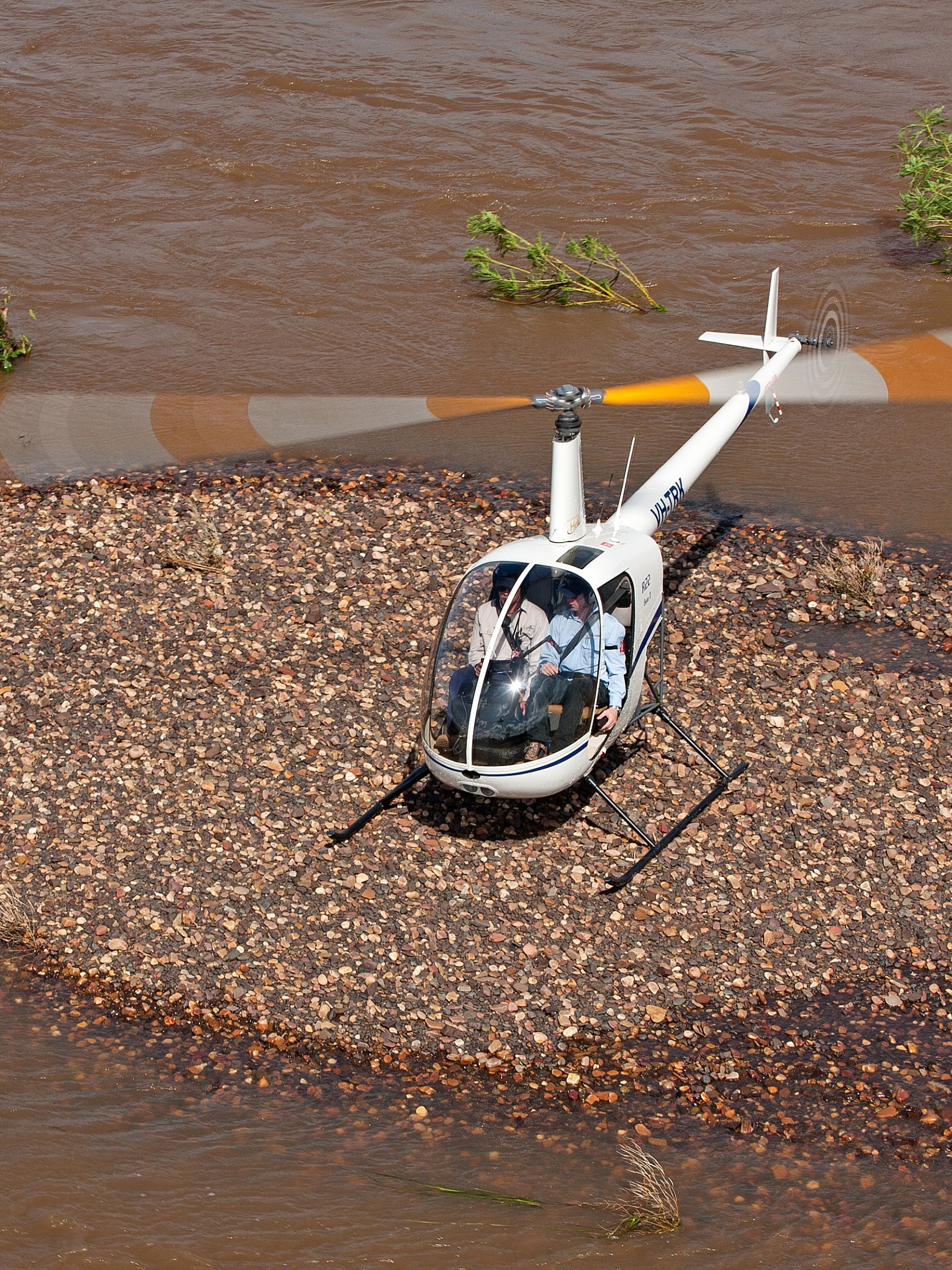 Helicopter parked on small rocky island in a muddy river.