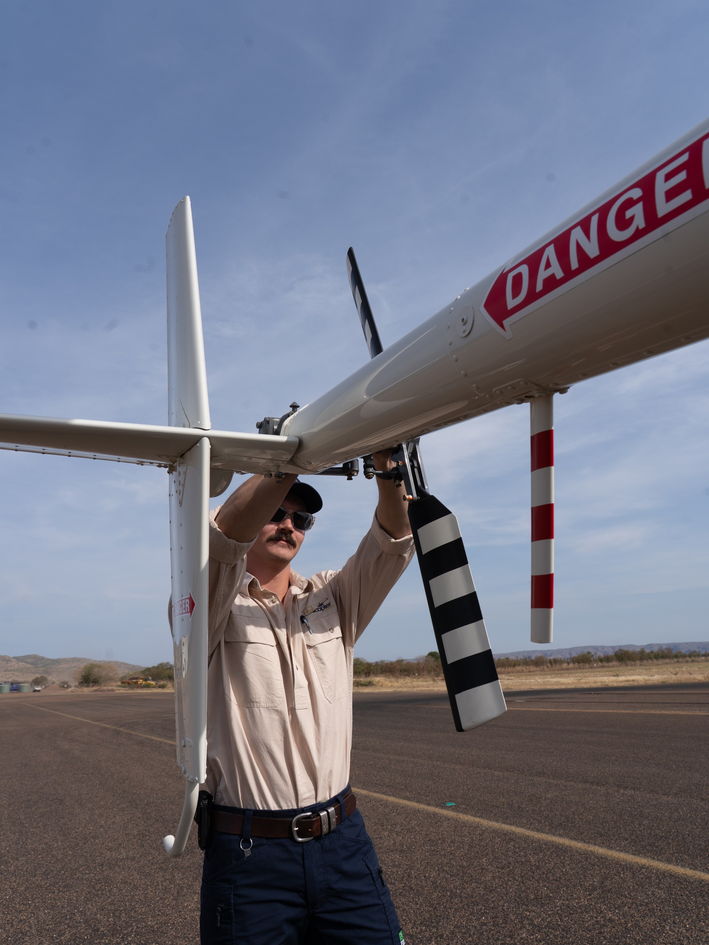 Person adjusts a white aircraft drone on a runway.