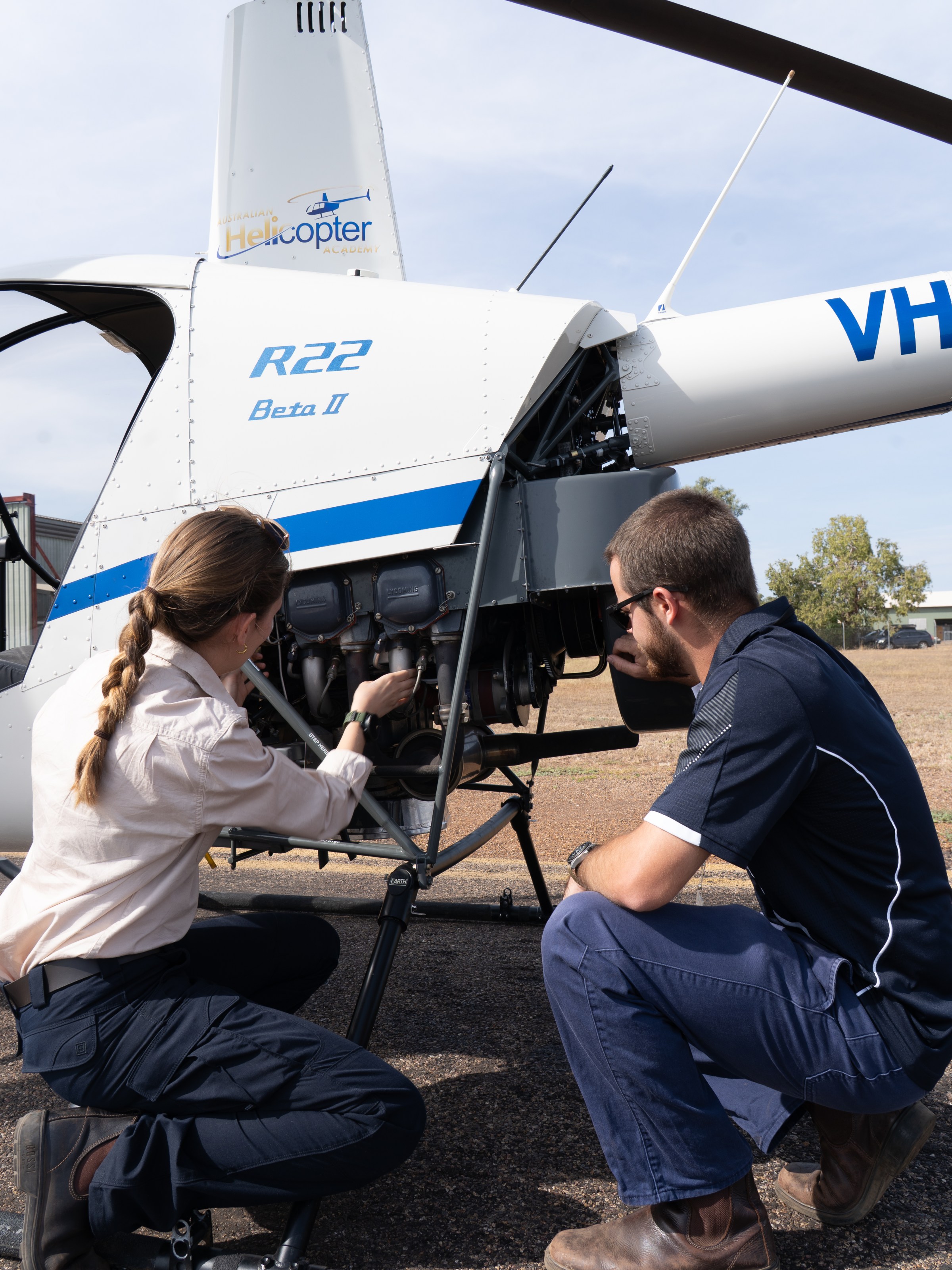 Two people inspect and work on a white helicopter on the ground.