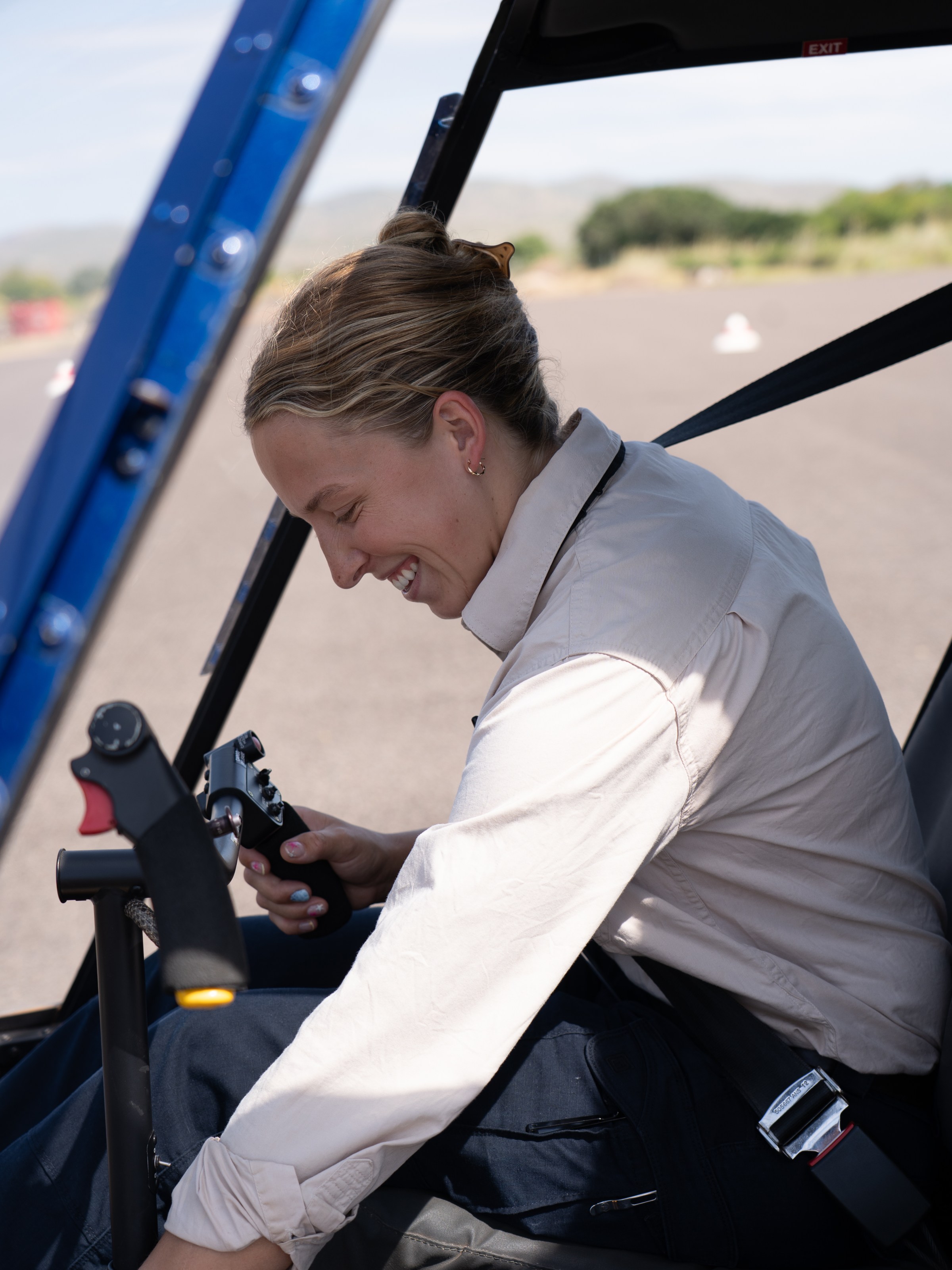 Person smiling and seated in a helicopter cockpit, holding controls.