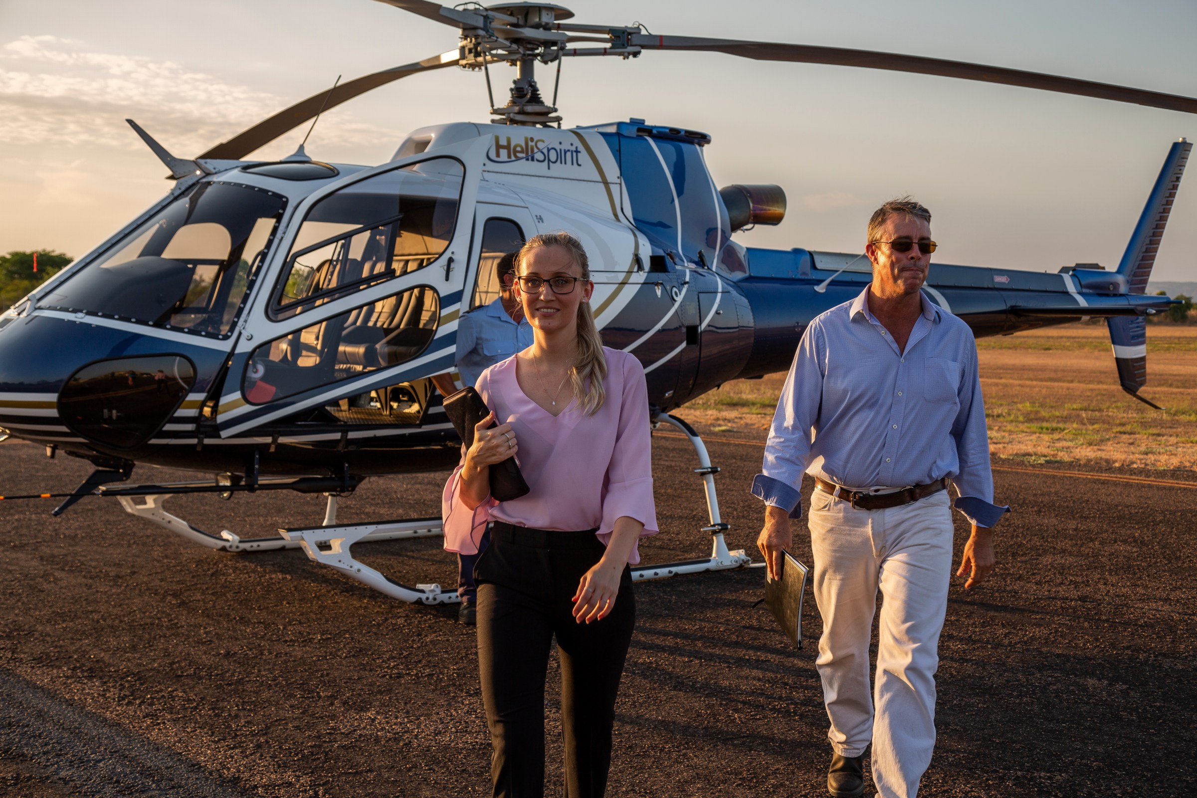 Two people walking away from a helicopter on a sunny day.