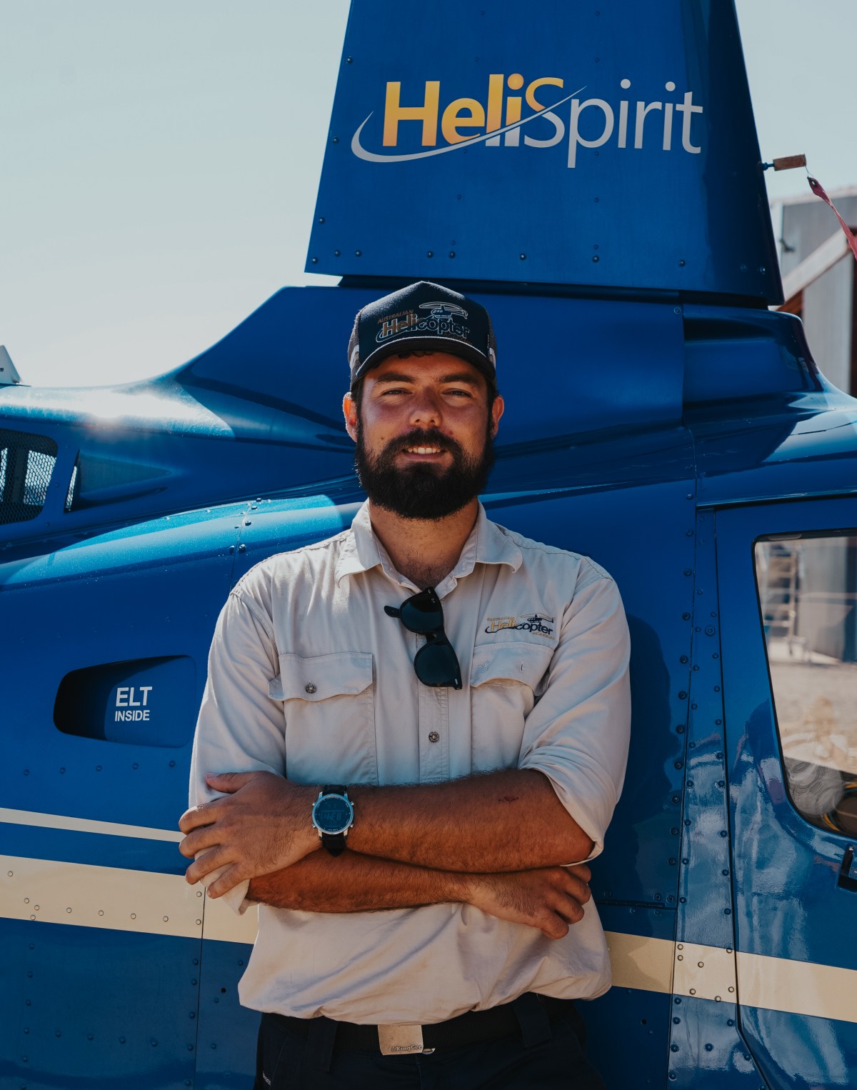 Man with beard stands in front of blue helicopter