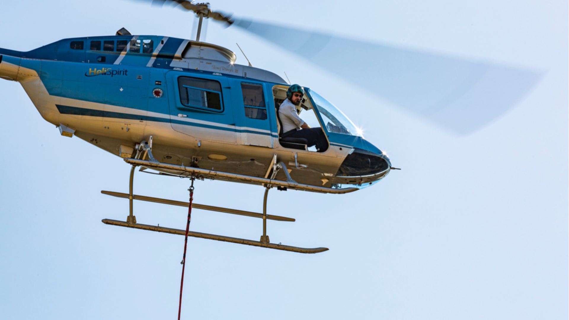 Blue helicopter in flight with person sitting in open door.