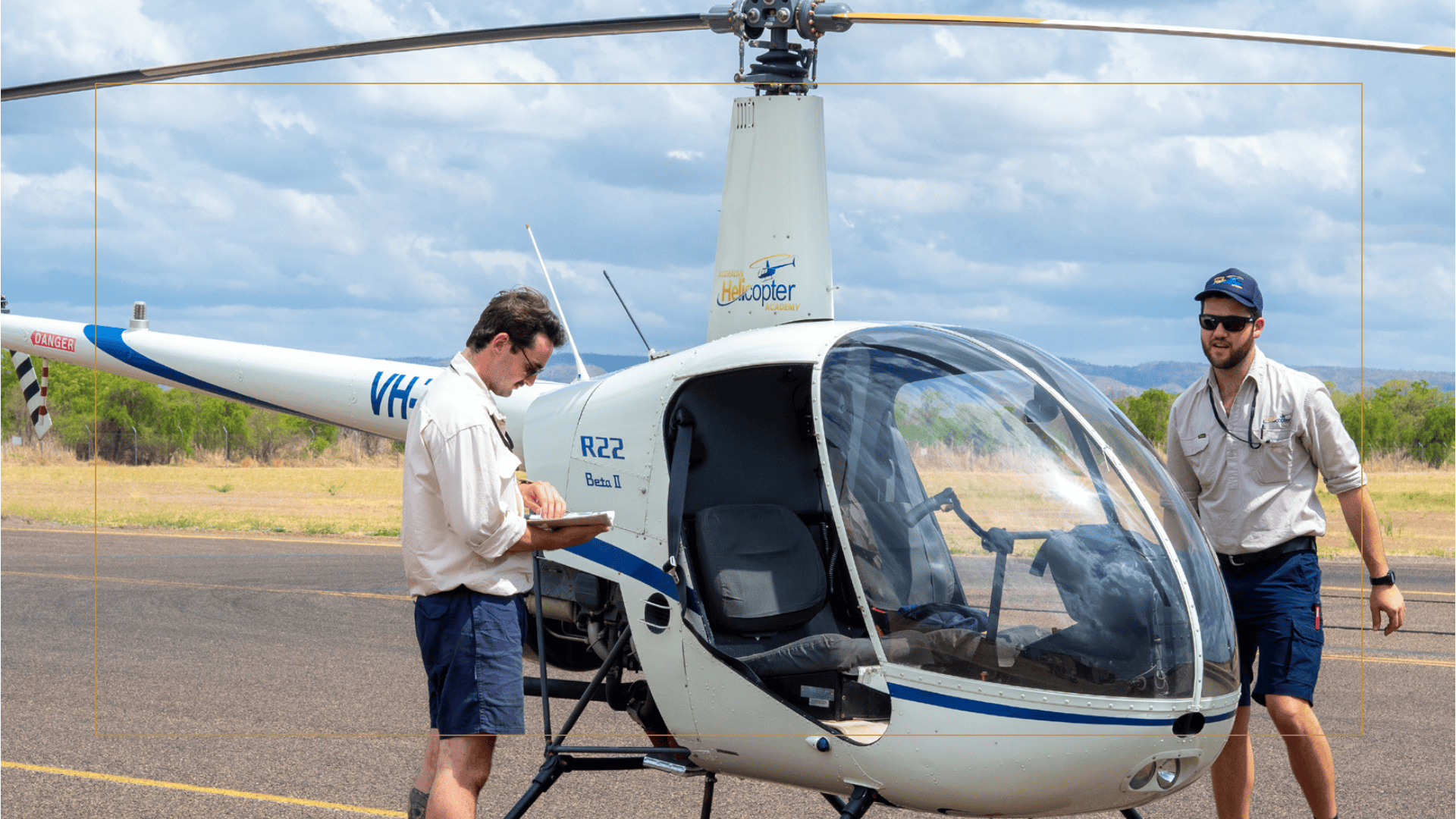 Two men with a helicopter on a runway under a cloudy sky.