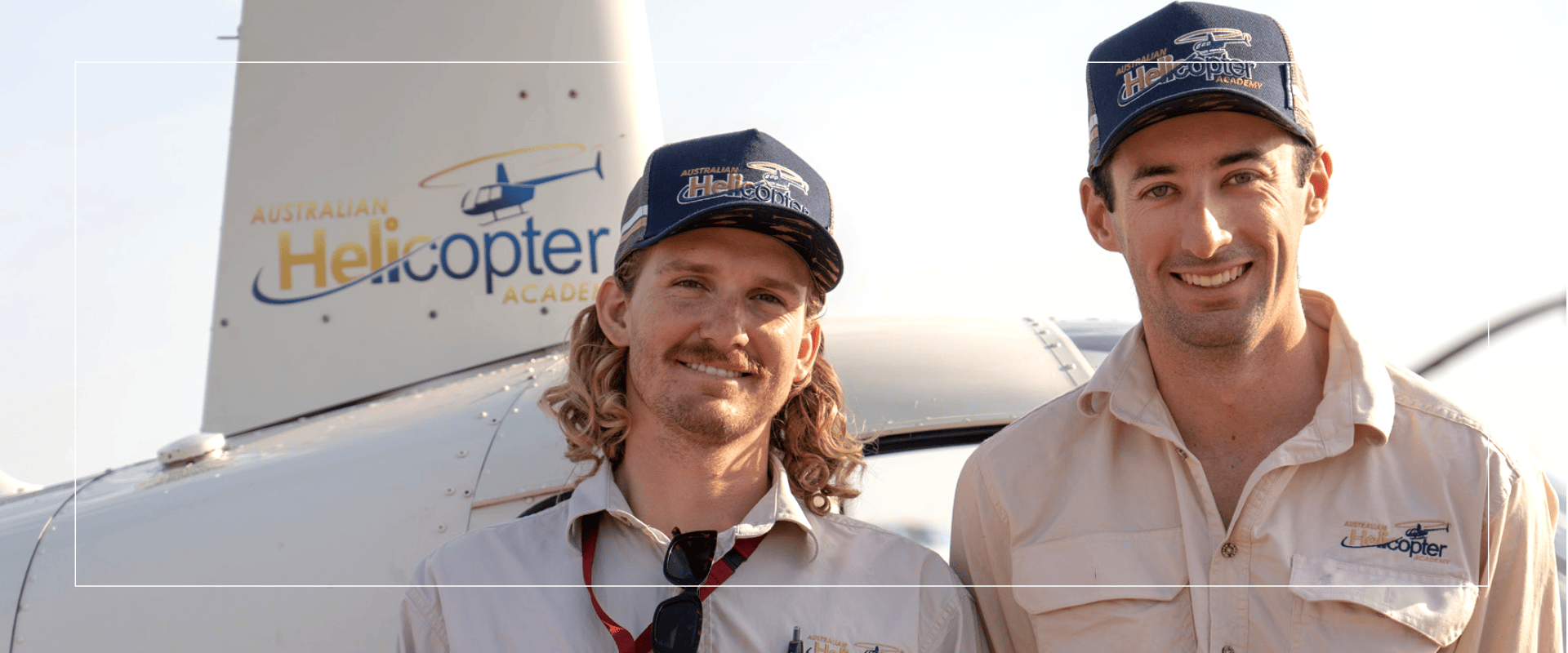 Two men in hats smiling in front of a helicopter.