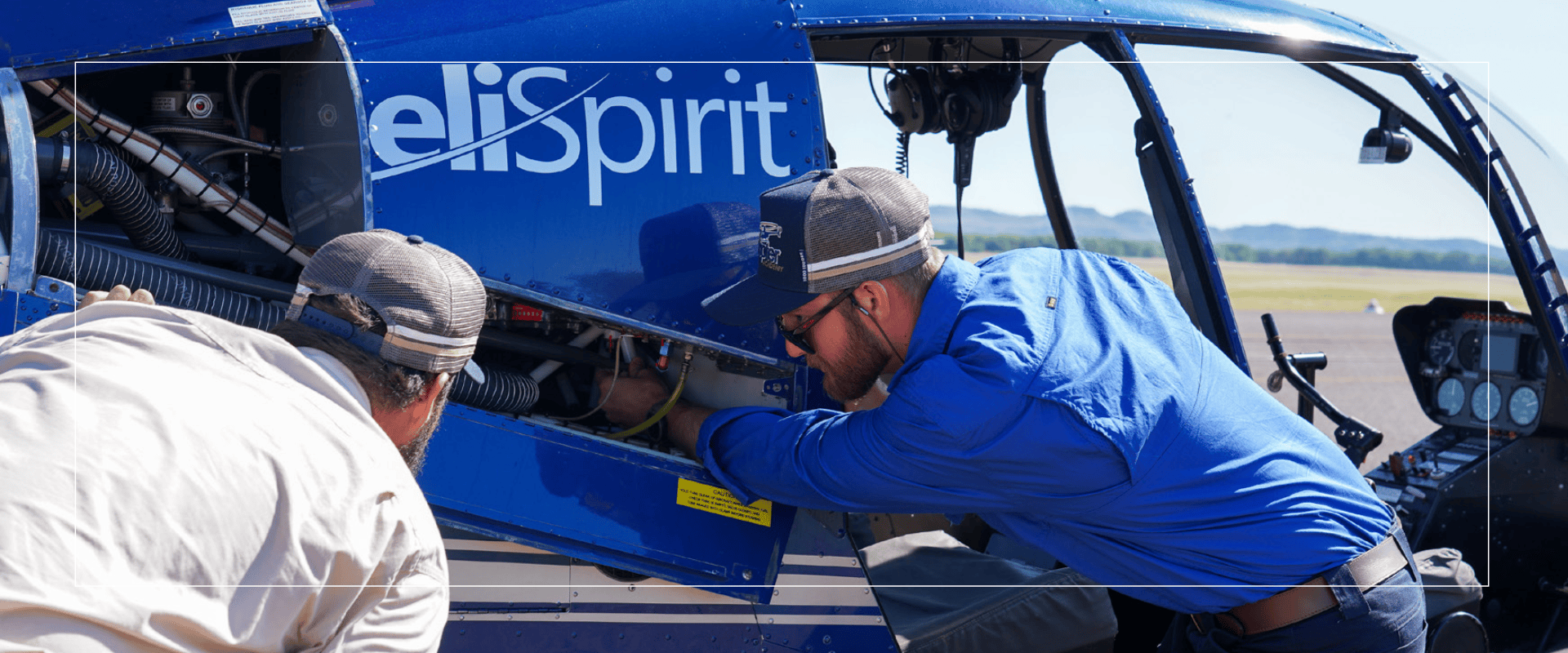 Two technicians inspect a helicopter engine on a sunny day.
