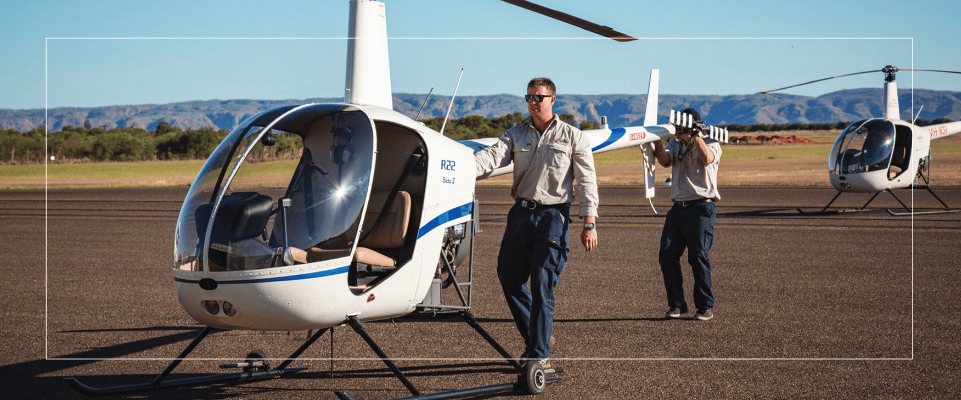 Two men walking near parked white helicopters on a sunny day.
