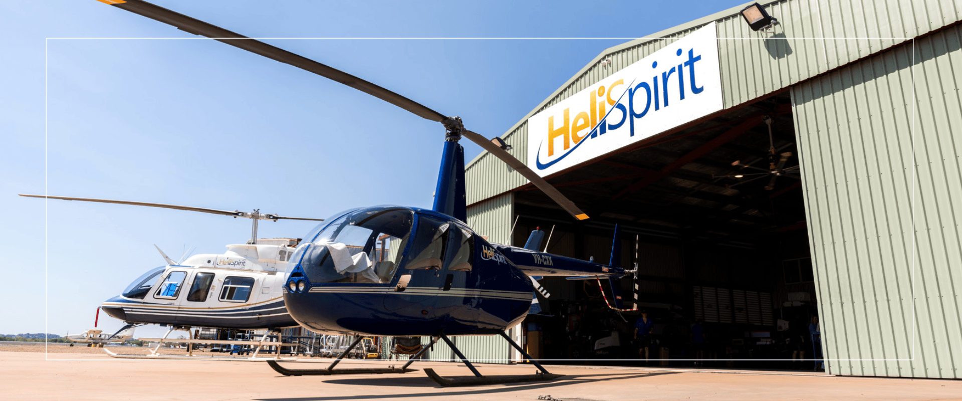Two helicopters near a hangar with 'HeliSpirit' sign.
