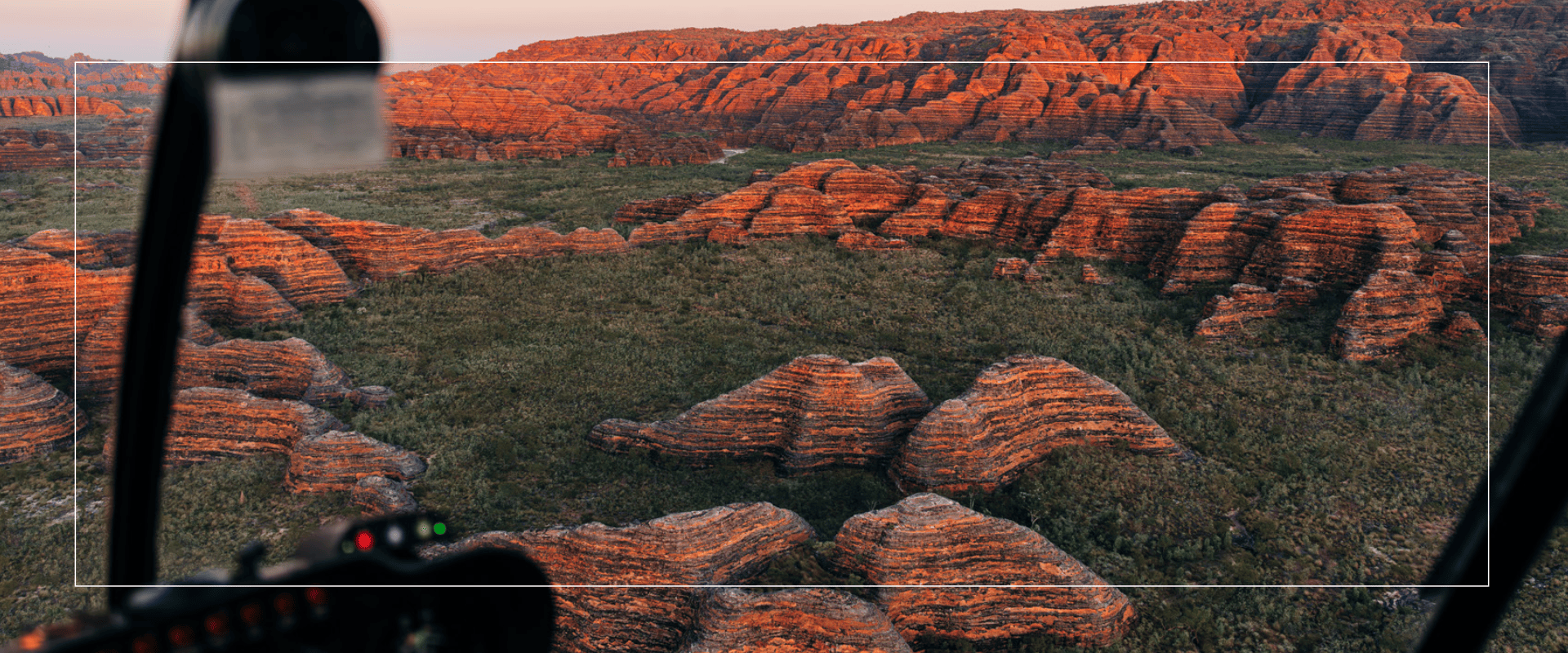 Aerial view of orange rock formations on grassy terrain at sunset.