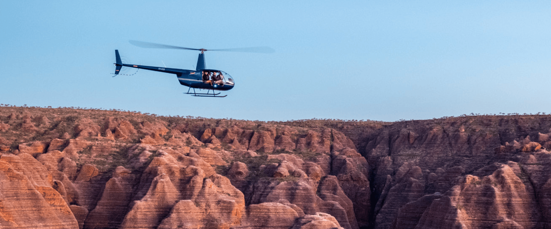 Helicopter flying over rugged red canyon landscape.