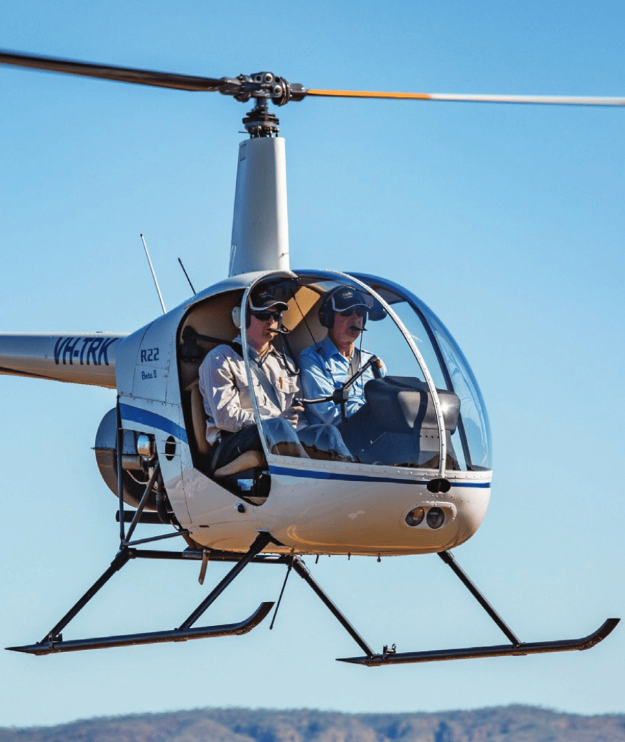 Two people in a flying white helicopter against a clear blue sky.