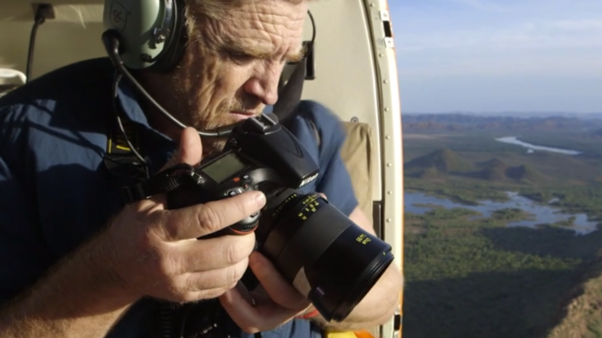 Person in headset using camera inside helicopter over scenic landscape.