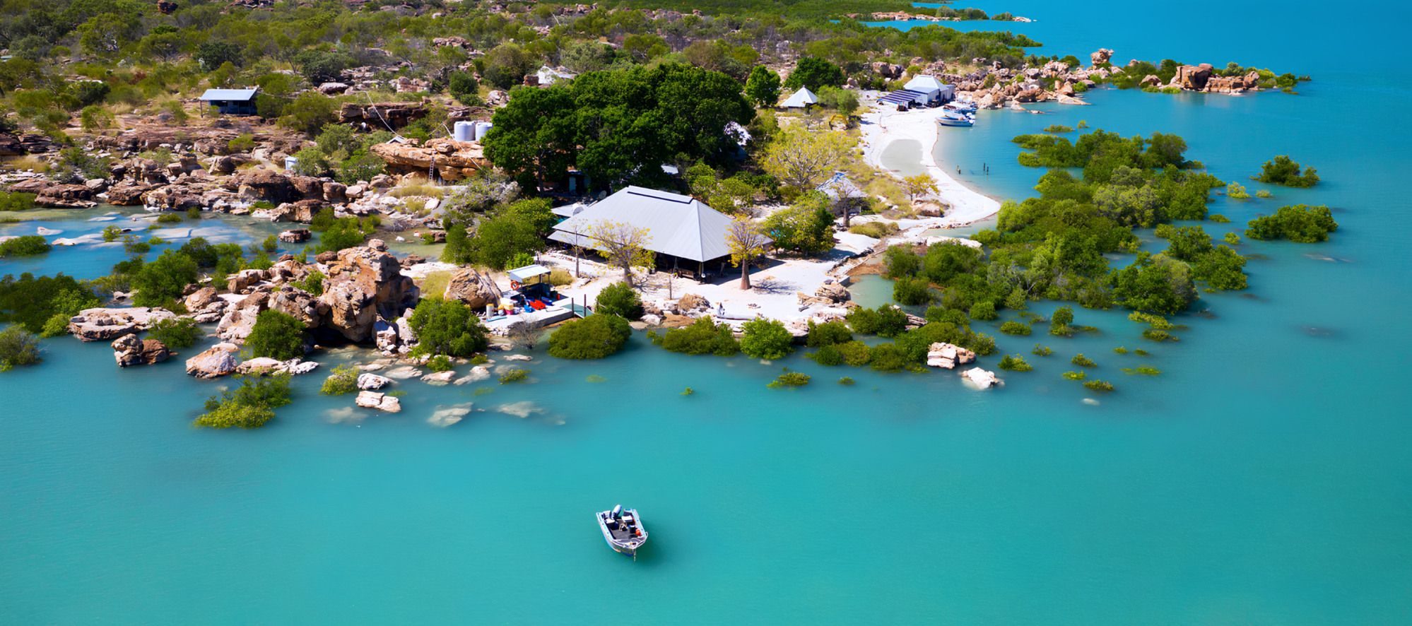 Aerial view of a small island with buildings, surrounded by turquoise water and greenery.