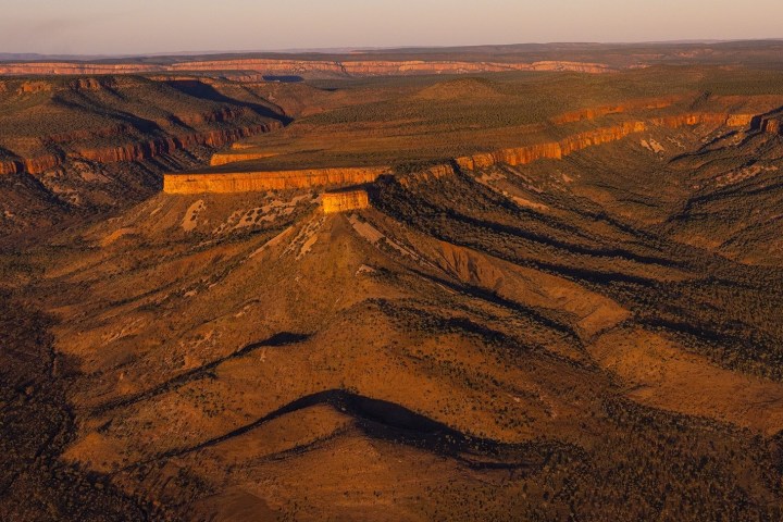 Aerial view of a vast desert landscape with mesas and long shadows.